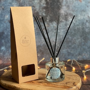 Könnte beinhalten: Ein brauner Karton mit einem ausgeschnittenen Fenster, neben einer durchsichtigen Glasflasche mit silbernem Deckel und schwarzen Diffusorstäbchen. Die Flasche trägt ein Etikett mit der Aufschrift "Valkyrie" und "Unsere Reisen sind es wert, versucht zu werden".