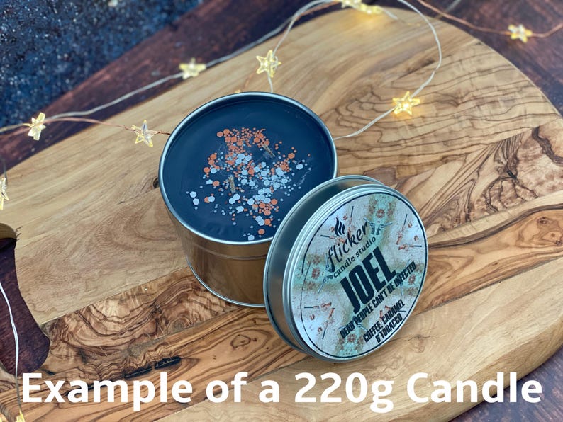 May include: A 220g candle in a silver tin with a black wax top. The candle is decorated with silver and orange glitter. The label on the tin reads "Flicker Candle Studio" and "JOEL DEAD PEOPLE CAN'T BE INFECTED COFFEE, CARAMEL & TOBACCO".
