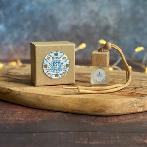 Könnte beinhalten: Eine kleine braune Schachtel mit einem weißen Etikett, auf dem "Flicker Candle Co. Nesta One World Not Fair Her People Get Mad No Room For Peace In Her Heart Chocolate Cake" steht. Neben der Schachtel befindet sich eine kleine Glasflasche mit einem Holzdeckel und einer braunen Schnur. Die Flasche hat ein weißes Etikett mit der Aufschrift "Flicker Candle Co."