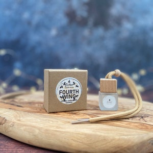 Może przedstawiać: Brązowe pudełko kartonowe z białą etykietą, na której widnieje napis "Flicker Candle Studio Fourth Wing Jasmine, Sandalwood, &amp; Bamboo" oraz mała szklana butelka z drewnianym korkiem i beżowym sznurkiem. Butelka jest oznaczona etykietą "Flicker".