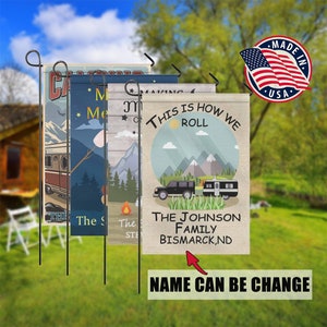 May include: Four colorful garden flags with a camping theme. The flags feature a camper, mountains, a campfire, and the text "This is how we roll". The bottom flag has the text "The Johnson Family Bismarck, ND".