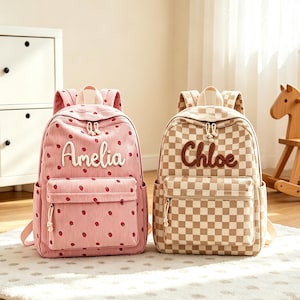 May include: Two backpacks with top handles and front zippered pockets. The left backpack is pink with a strawberry pattern and the name Amelia in white script. The right backpack features a beige and white checkerboard pattern with the name Chloe in brown.