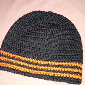 Puede incluir: Gorro de punto negro con una ancha franja naranja alrededor de la parte inferior.