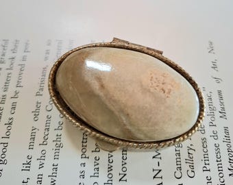 May include: A small, oval-shaped trinket box with a gold-toned metal frame and a light brown, marbled stone top.