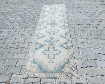 May include: A rectangular, vintage-style rug with a cream-colored background and intricate geometric patterns in shades of blue and beige. The rug is placed on a gray brick surface, showcasing its design.