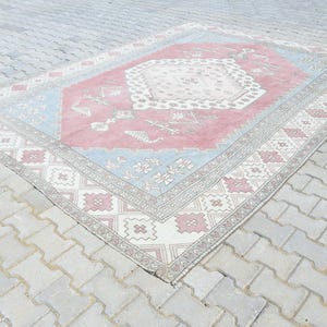 May include: A vintage rug with a pink, blue, and white geometric pattern. The rug has a faded, distressed look, giving it a unique and charming character.