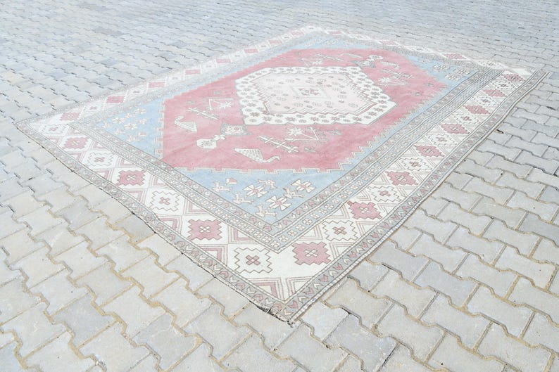 May include: A vintage rug with a pink, blue, and white geometric pattern. The rug has a faded, distressed look, giving it a unique and charming character.