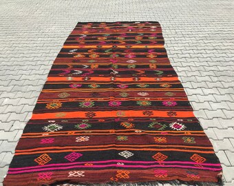 Pode incluir: Um tapete longo e estreito, tecido à mão, com um padrão geométrico colorido. O tapete é feito de lã e tem franjas em ambas as extremidades. As cores do tapete são vermelho, laranja, amarelo, verde, azul e preto.