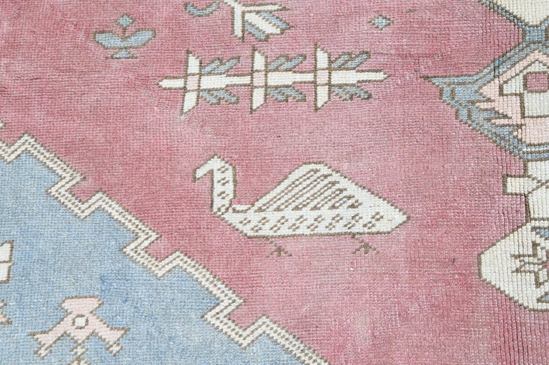 May include: A pink and blue rug with a geometric pattern. The rug features a stylized bird design in the center.