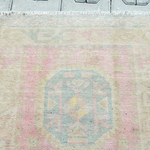 May include: A rectangular rug with a faded, vintage appearance. The rug features a central design in shades of blue, pink, and yellow, surrounded by a beige border. The rug's edges have a fringed detail.