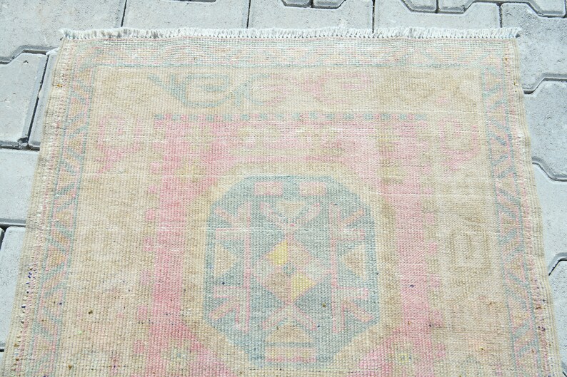 May include: A rectangular rug with a faded, vintage appearance. The rug features a central design in shades of blue, pink, and yellow, surrounded by a beige border. The rug's edges have a fringed detail.