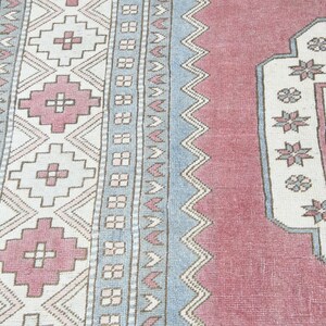 May include: A vintage rug with a pink and blue geometric pattern. The rug has a central medallion with a floral design.