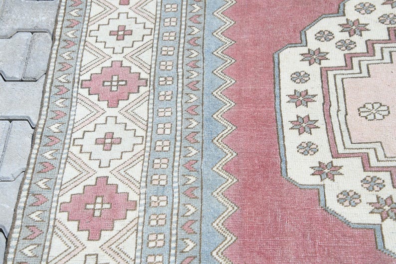 May include: A vintage rug with a pink and blue geometric pattern. The rug has a central medallion with a floral design.