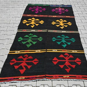 Könnte beinhalten: Ein schwarzer und bunter Teppich mit einem geometrischen Muster aus Schneeflocken. Der Teppich hat einen Fransenrand und ist aus Wolle.