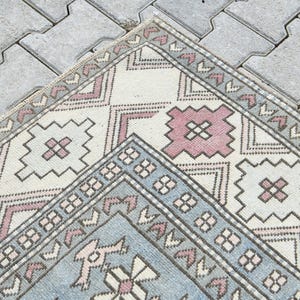 May include: A vintage Turkish rug with a geometric pattern in shades of pink, blue, and white. The rug has a distressed look and is perfect for adding a touch of bohemian style to any room.
