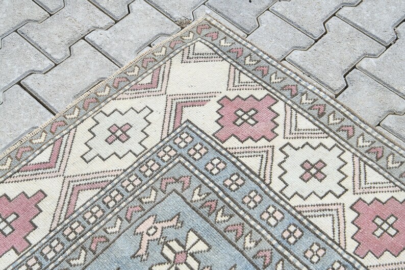 May include: A vintage Turkish rug with a geometric pattern in shades of pink, blue, and white. The rug has a distressed look and is perfect for adding a touch of bohemian style to any room.