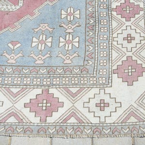May include: Close-up of a vintage rug with a light blue, pink, and white geometric pattern. The rug has a fringe border and is made of wool.