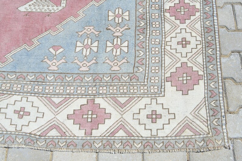 May include: Close-up of a vintage rug with a light blue, pink, and white geometric pattern. The rug has a fringe border and is made of wool.