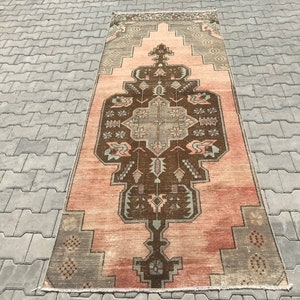 May include: A vintage Turkish rug with a traditional geometric pattern in shades of brown, pink, and grey. The rug has a faded, distressed look, giving it a unique and antique feel.