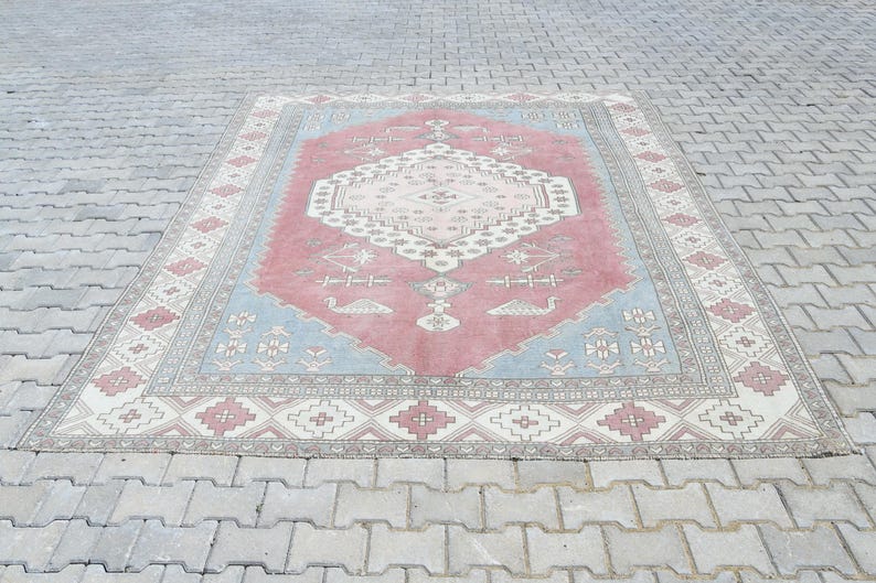 May include: A vintage rug with a light blue, pink, and cream color scheme. The rug has a traditional geometric pattern with a central medallion.