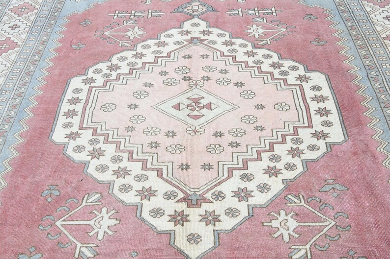 May include: A pink and white patterned rug with a central diamond shape. The rug has a traditional design with intricate details.