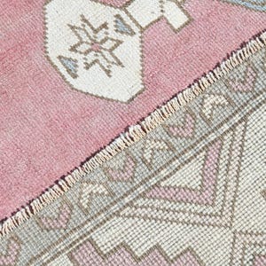 May include: Close-up of a pink and white patterned rug with a fringe border. The rug has a geometric design with a repeating pattern of triangles and squares.