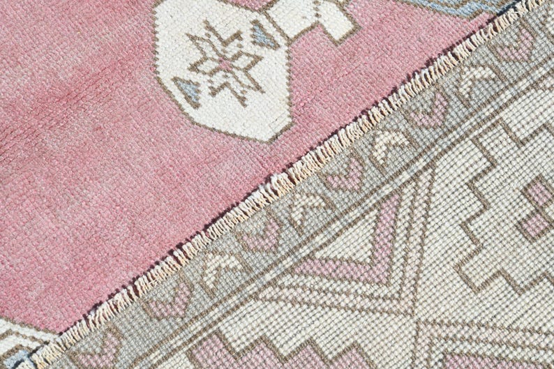 May include: Close-up of a pink and white patterned rug with a fringe border. The rug has a geometric design with a repeating pattern of triangles and squares.