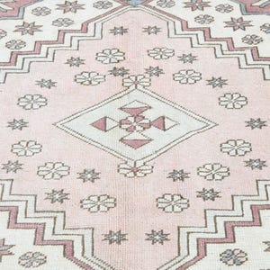 May include: A pink and white rug with a geometric pattern. The rug has a central diamond shape with a smaller diamond inside. The rug is decorated with stars and flowers.