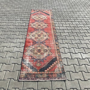 May include: A vintage red, blue, and cream runner rug with a traditional Persian design. The rug has a distressed look and is made of wool.