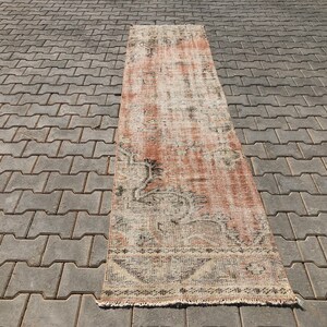 May include: A rectangular rug with a distressed, vintage appearance. The rug has a faded colour palette of reds, beige, and black. It features geometric and floral patterns, and has a fringed edge. The rug is suitable for a hallway.