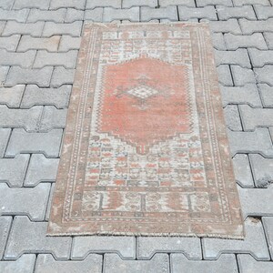 Puede incluir: Alfombra rectangular de estilo vintage con un medallón central de color coral y detalles crema. La alfombra presenta bordes detallados en tonos marrón y beige, con un aspecto envejecido, y mide aproximadamente 120 cm x 70 cm.