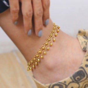 May include: A gold anklet with a delicate chain and dangling beads. The anklet is worn on a person's ankle.