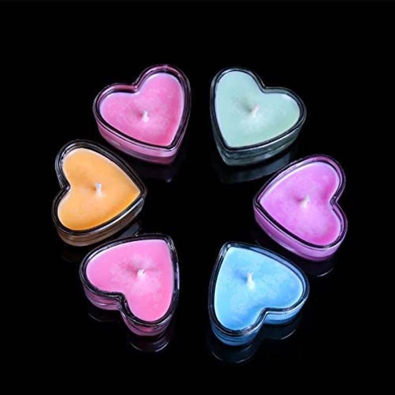 Puede incluir: Seis velas en forma de coraz&oacute;n de varios colores, incluyendo rosa, naranja, verde, azul y morado. Las velas est&aacute;n dispuestas en c&iacute;rculo sobre un fondo negro.