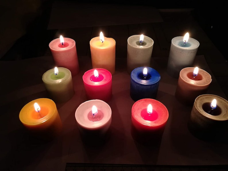 Puede incluir: Una colecci&oacute;n de 12 velas coloridas, cada una con un tono diferente, incluyendo amarillo, verde, rosa, rojo, azul y blanco. Las velas est&aacute;n todas encendidas y proyectan un brillo c&aacute;lido.