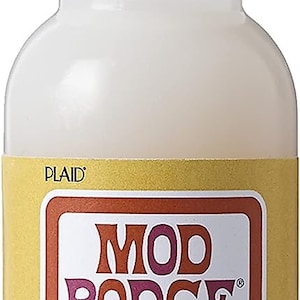 May include: A clear plastic bottle of Mod Podge Dimensional Magic glue, with a yellow label that says "Mod Podge" in a retro font. The label also says "Dimensional Magic" and "Adds Clear 3D Accents". The bottle is 2 fl oz (59 ml).