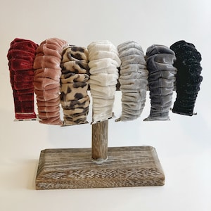 May include: A set of eight watch bands displayed on a wooden stand. The bands are made of velvet and come in a variety of colours and patterns, including red, pink, leopard print, white, grey, and black.