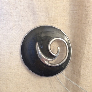 May include: A black and silver metal decorative accent with a swirling design. The accent is attached to two silver cords.