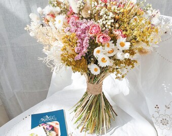 May include: A bouquet of dried flowers in shades of pink, white, and yellow. The bouquet is tied with twine and includes dried roses, daisies, and grasses.