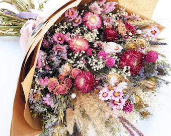 Könnte beinhalten: Ein Strauß getrockneter Blumen in Rosa-, Lila- und Weißtönen, verpackt in braunes Papier. Der Strauß enthält getrocknete Rosen, Lavendel und andere Wildblumen.