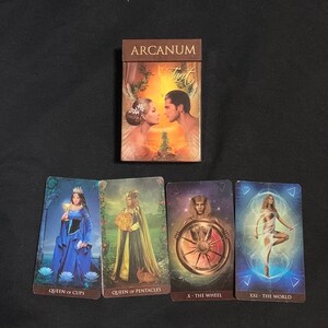 Pode incluir: Caixa de baralho de tarot com o t&iacute;tulo "Arcanum Tarot" e quatro cartas de tarot: Rainha de Copas, Rainha de Pent&aacute;culos, A Roda da Fortuna e O Mundo.