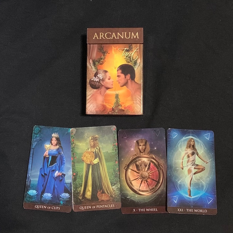 Pode incluir: Caixa de baralho de tarot com o t&iacute;tulo "Arcanum Tarot" e quatro cartas de tarot: Rainha de Copas, Rainha de Pent&aacute;culos, A Roda da Fortuna e O Mundo.