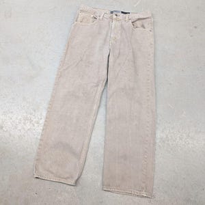 May include: A pair of light tan denim jeans featuring a classic five-pocket design, a button and zipper fly closure, and a straight-leg cut. The pants have visible belt loops at the waistband and tonal stitching throughout the fabric construction.