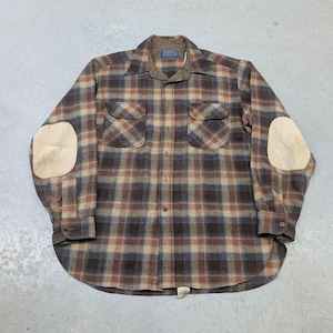 May include: A long-sleeve button-down shirt featuring a brown, tan, and blue plaid pattern. The shirt includes two chest pockets with flaps, a pointed collar, and light tan suede-like elbow patches on each sleeve. A label is visible at the neck.