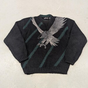 May include: Black knitted sweater with a green and white eagle graphic. The sweater has a crew neck and long sleeves. The brand name "Montello" is printed on the tag.
