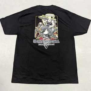 以下が含まれることがあります： 「攻殻機動隊 STAND ALONE COMPLEX」のアニメキャラクターが描かれた黒いTシャツ。キャラクターは銃を持っており、他のキャラクターに囲まれています。グラフィックの下には「攻殻機動隊 STAND ALONE COMPLEX」の文字が印刷されています。