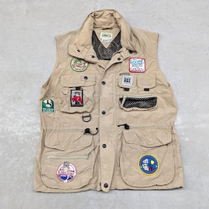 May include: A tan utility vest with multiple pockets and zipper closures. The vest has several patches sewn on the front, including a "Bubba Gump" patch, a "Hiker's Canyon" patch, and a "The Lodge at Kohler" patch.