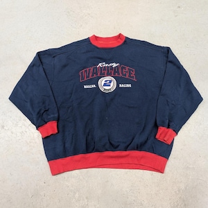 May include: Navy blue sweatshirt with red trim at the collar and cuffs. The front features the name "Rusty Wallace" in red arched lettering above a circular emblem with the number "2" and the words "NASCAR Racing".
