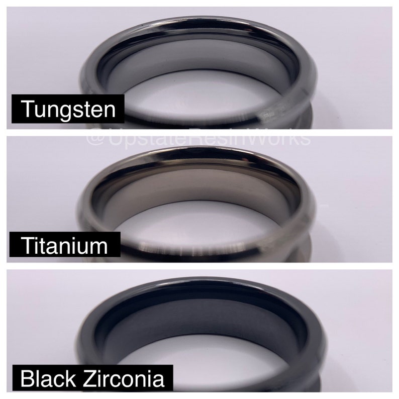 May include: Close-up of three rings, each made of a different material: tungsten, titanium, and black zirconia. The rings are all black and have a polished finish.