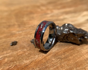 Peut inclure: Gros plan d'une bague en carbure de tungstène gris foncé avec un incrustation rouge et or. La bague est posée sur une surface en bois.