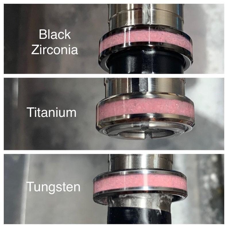 May include: Close-up of three metal rings with a pink band. The rings are labelled "Black Zirconia", "Titanium", and "Tungsten".